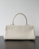 A structured cream-colored pebbled leather handbag with a top handle, resting on a dark surface against a plain light gray wall.